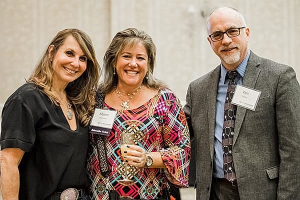 Three people smiling at a formal event.