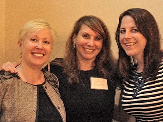Three smiling women posing together indoors.