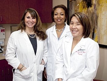 Three female doctors smiling in clinic setting.