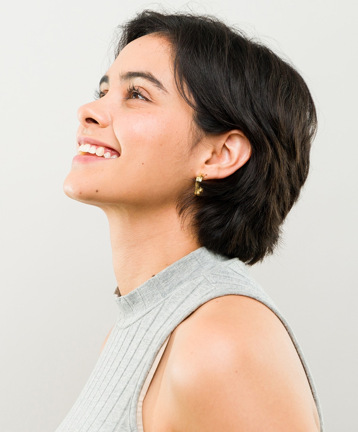 Woman smiling with short hair, wearing earrings.