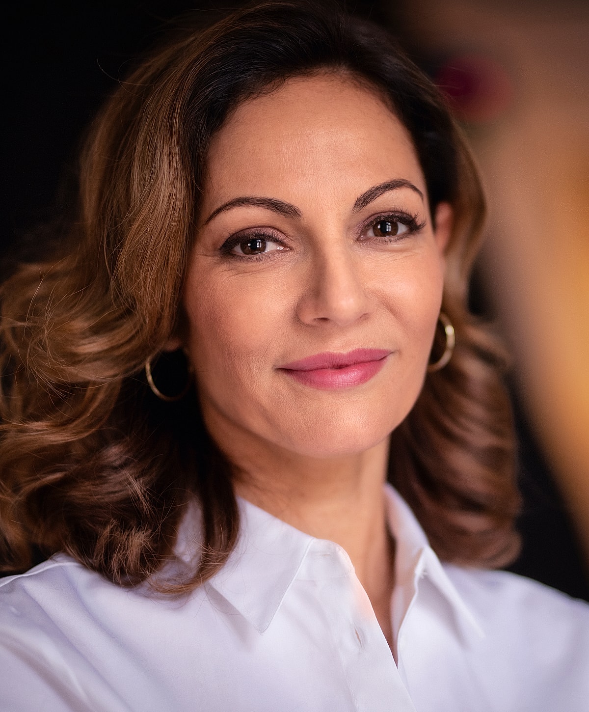 Woman with curly hair smiling in white shirt.