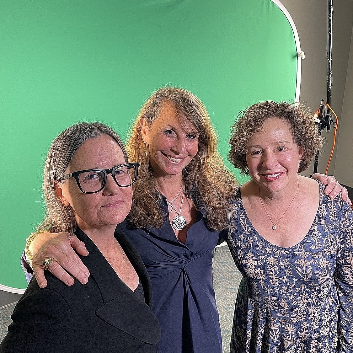 Three women smiling in front of green screen.