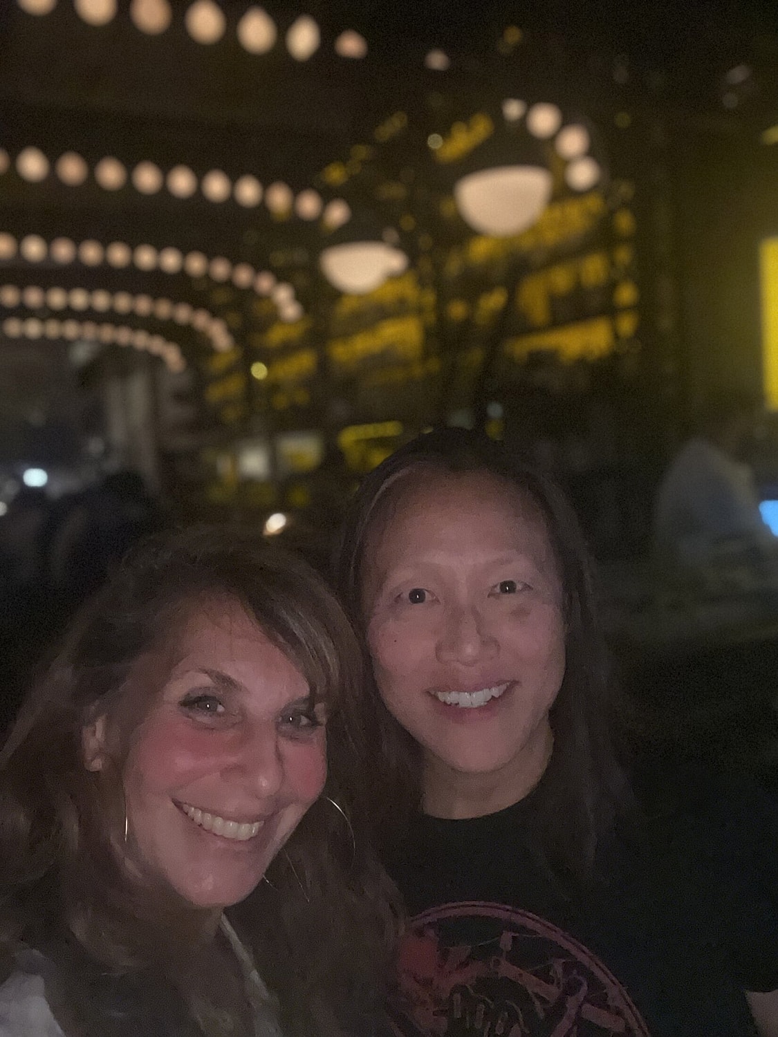 Two friends smiling in a dimly lit venue.