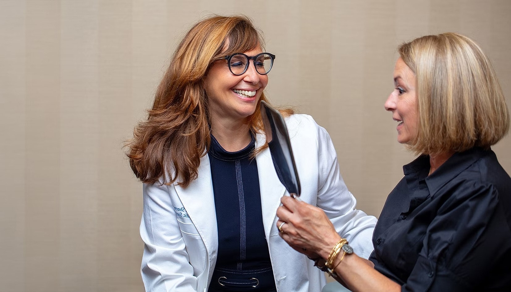 Two women smiling and interacting in office setting.